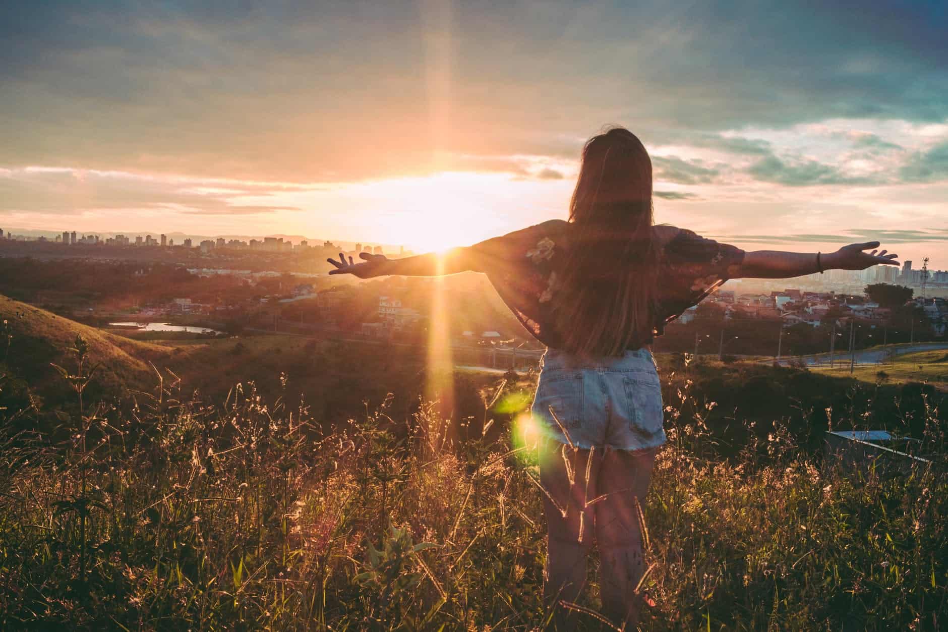 Woman standing with arms open at sunset, embracing hope and freedom.