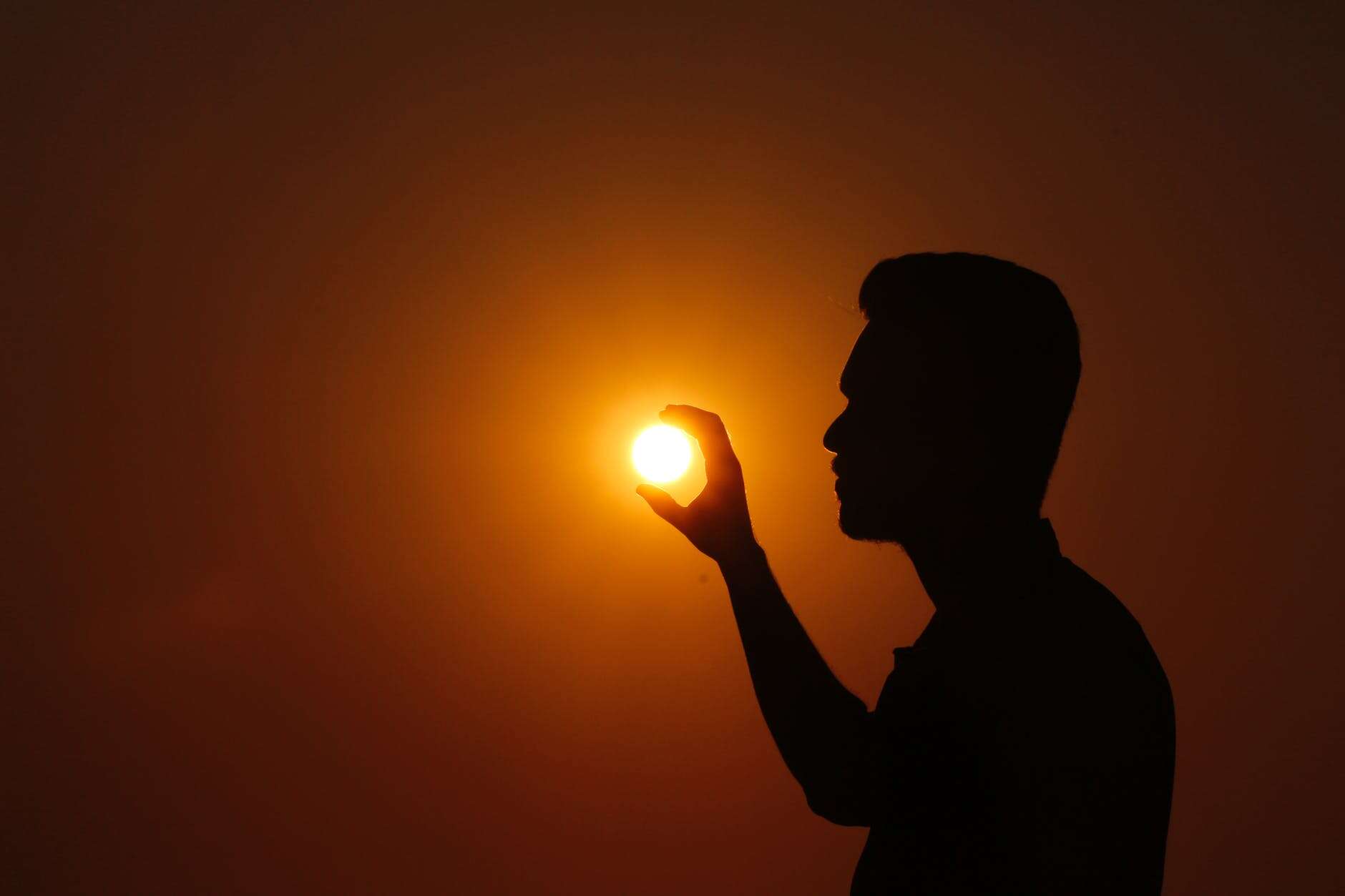 Silhouette of a person holding the sun at sunset, symbolizing conflict resolution.