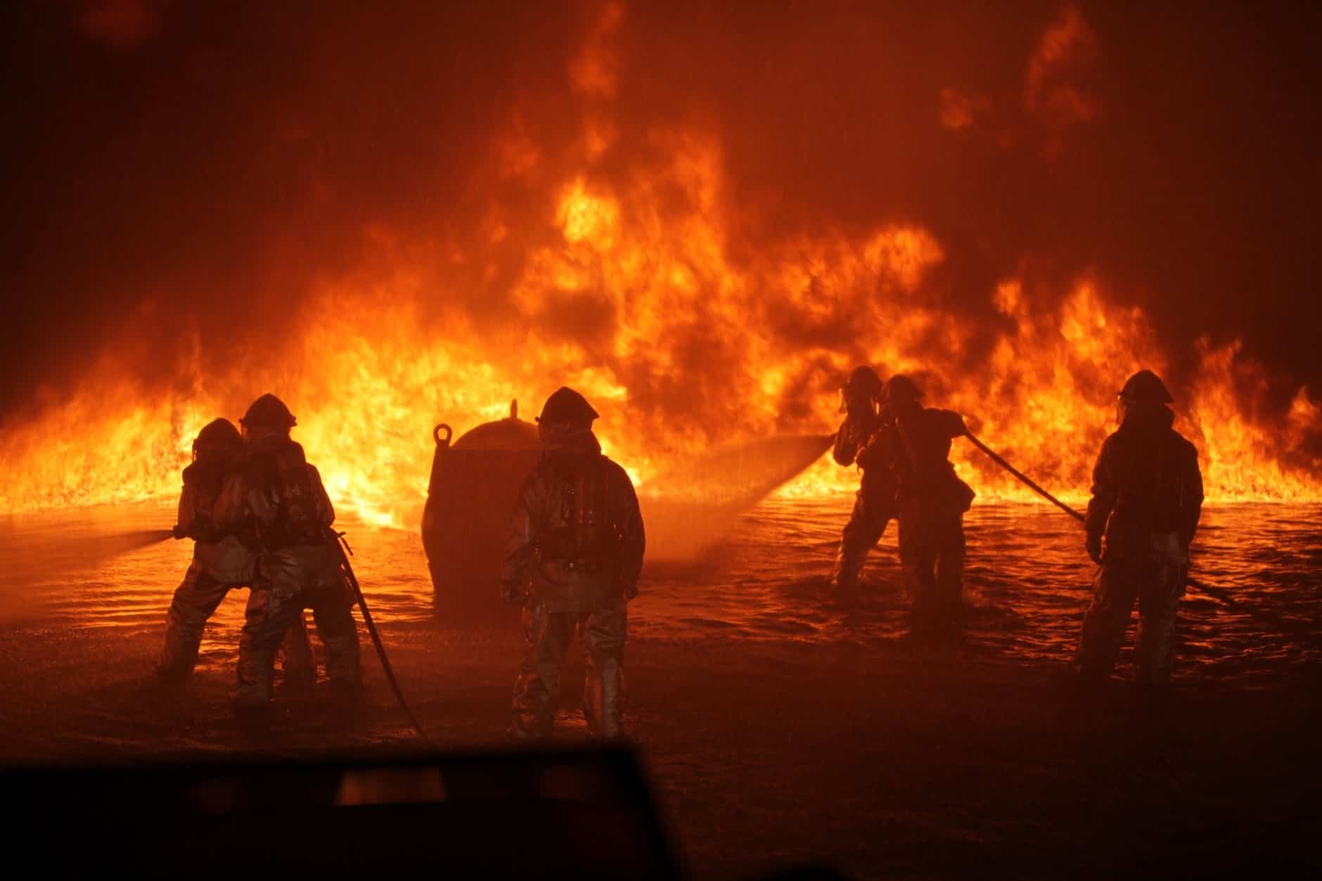 Firefighters fighting a large fire at night with flames in the background.