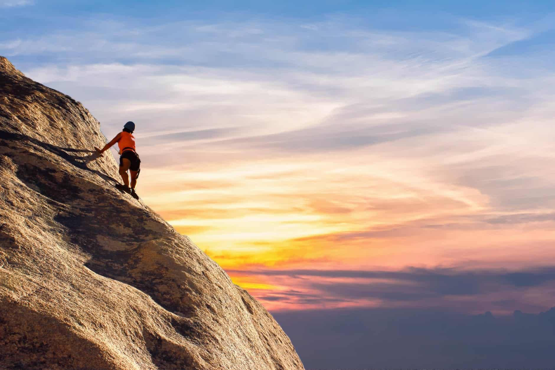 Person climbing steep rock face at sunset, symbolizing resilience and conflict resolution.