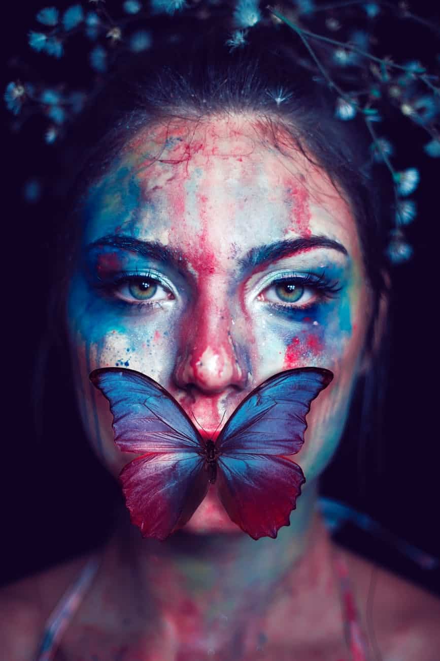 Woman with colorful face paint and butterfly on lips, artistic portrait.