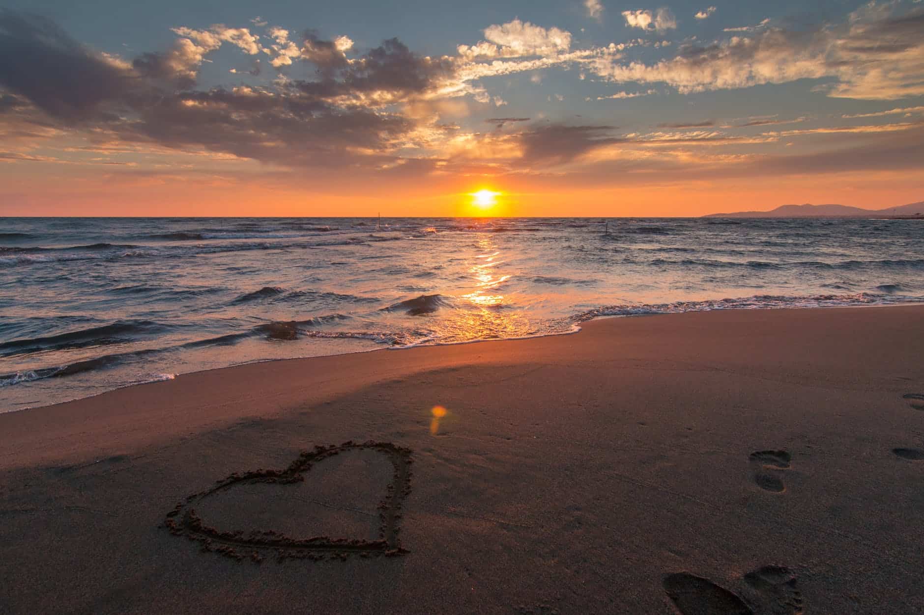 Beautiful sunset at the beach with a heart-shaped sand drawing and footprints.