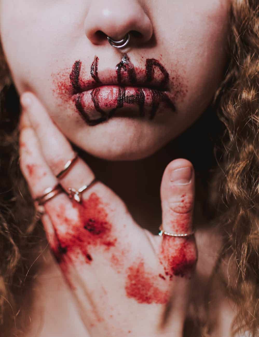 Close-up of a woman with smeared lipstick and bloodstained hand, symbolizing emotional conflict.